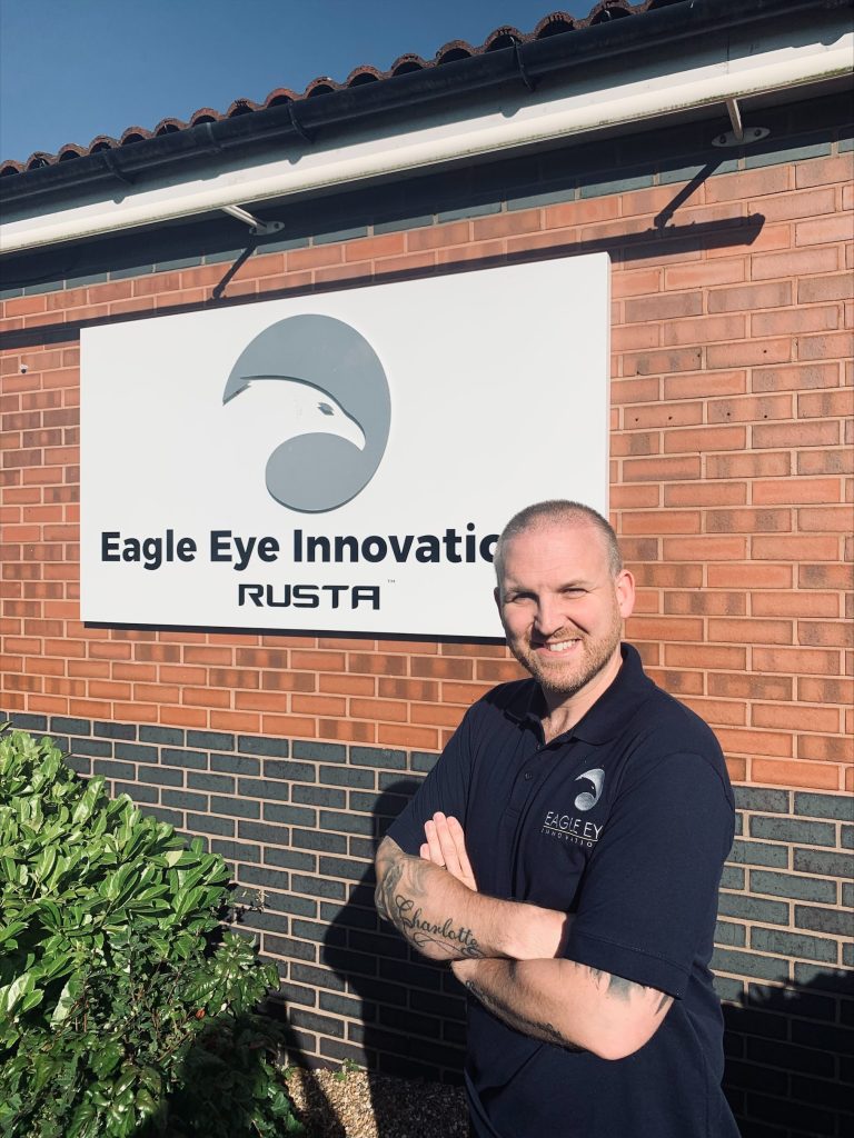 Image of man with folded arms stood in front of Eagle Eye Innovations RUSTA sign.