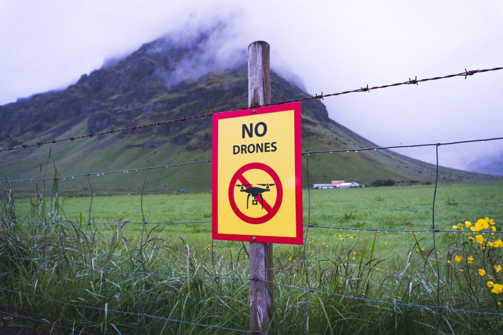 'No Drones' sign on barbed fence in front of field.