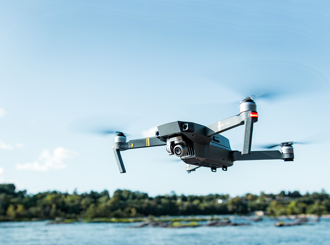 Close up image of drone flying over water with trees in the background.