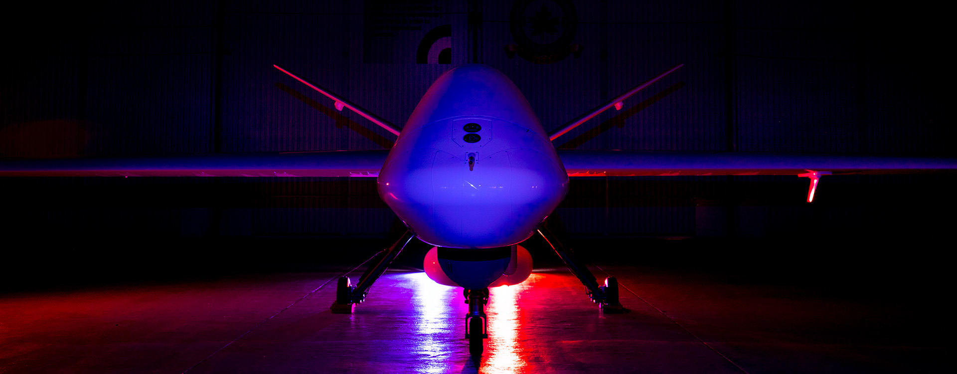 Protector aircraft on a dark runway facing forward with blue and red lighting behind it.