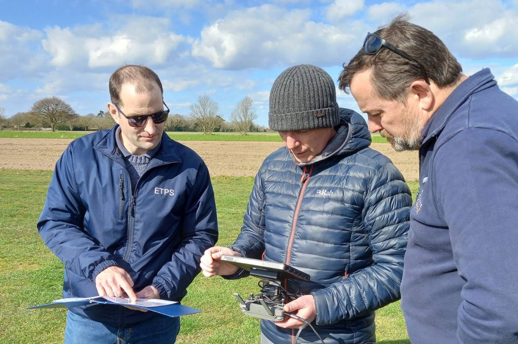 Image of three men looking at pieces of paper with drone training information on them.