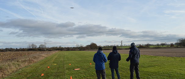 3 people looking at drone flying in the air in front of them.