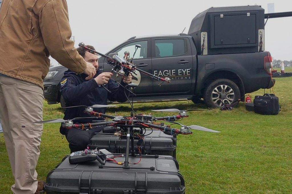 Image of men testing new drone in a field. Eagle Eye Innovations branded vehicle in the background.