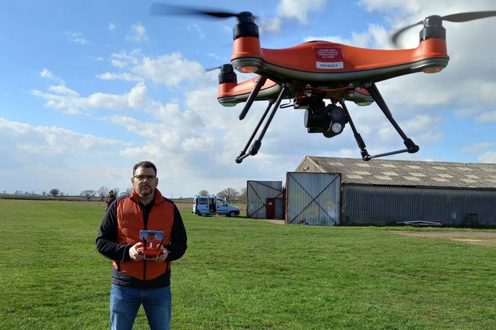 Man in a field flying a drone towards the camera.