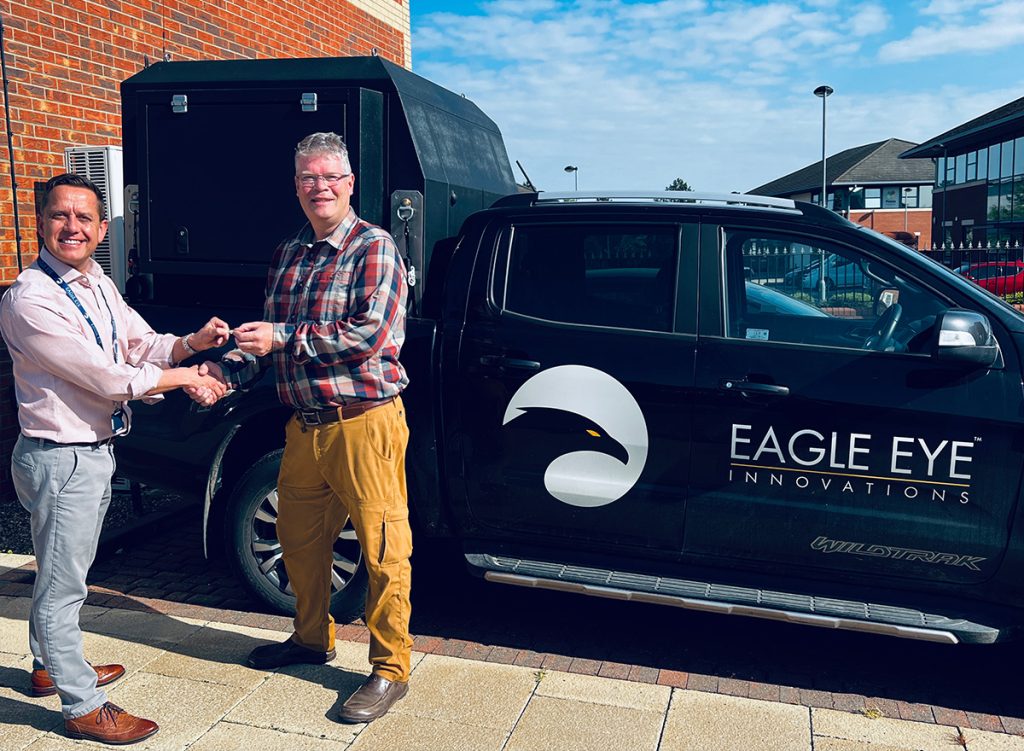Man handing an award to another man stood in front of Eagle Eye Innovations branded truck.