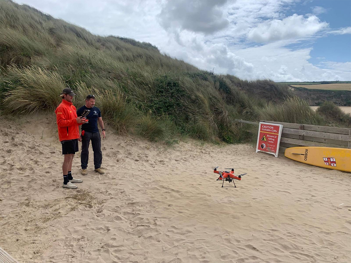 Two men lifeguarding on beach with drone hovering above the sand.