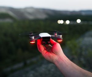 Hand holding a DJI Mini drone with red lights and mountains in the background.